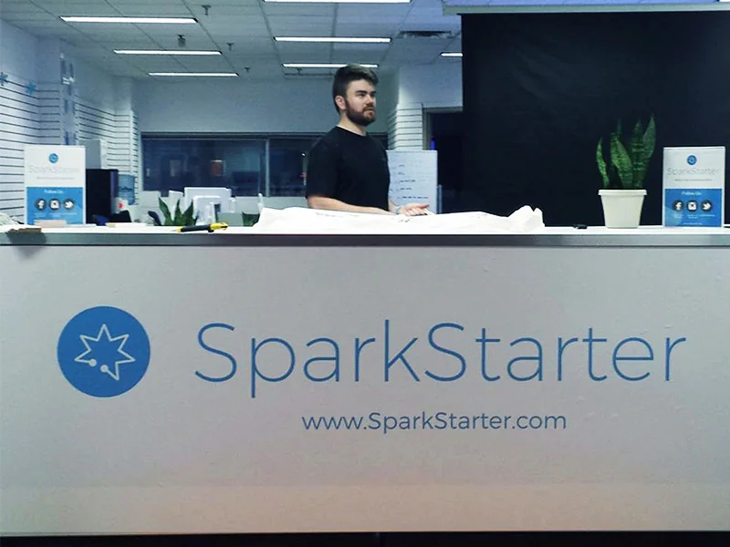 SparkStarter branding applied to an event booth desk, with the logo and wordmark printed large across the front panel
